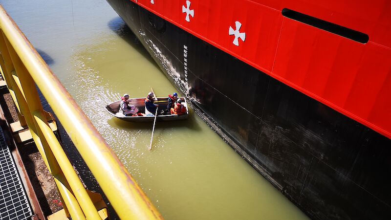 Men in a small row boat measure draft marks on the hull of the Nuyina.