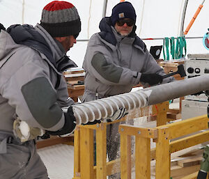 Two men removing an ice core from a drill barrel