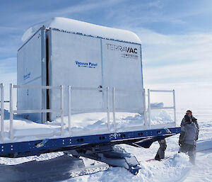 Expeditioners standing in the snow next to a large (about 3 m square) box