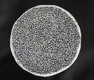 Close up of circular piece of ice core with bubbles on a black background