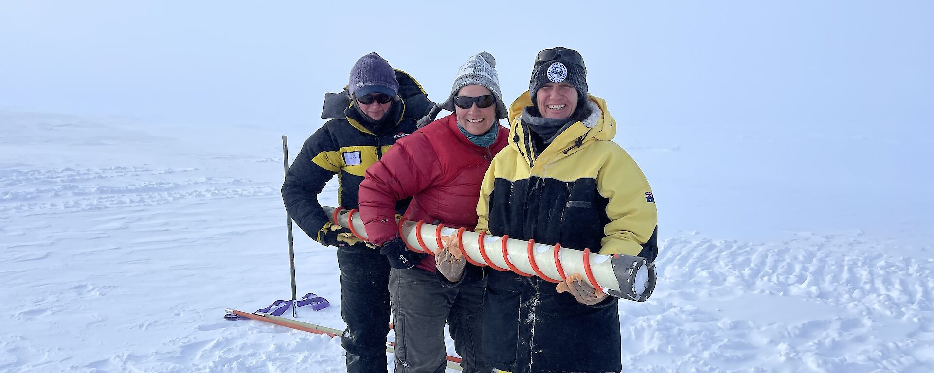 3 expeditioners hold a long tube in an icy landscape.