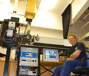 Dr John French sits in the optics lab, next to the measuring instrument, the Hydroxyl Spectrometer.