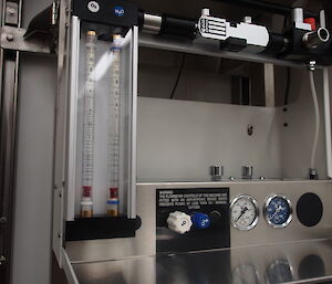 An anaesthetic machine with glass cylinders, flow controls and dials for administration of gases.