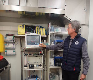 Dr Clive Strauss points to the anaesthetic monitor above the simple anaesthetic machine. A cardiac monitor and defibrillator are in the yellow pack on the shelf above, while the blue screen of the transport ventilator can be seen below.
