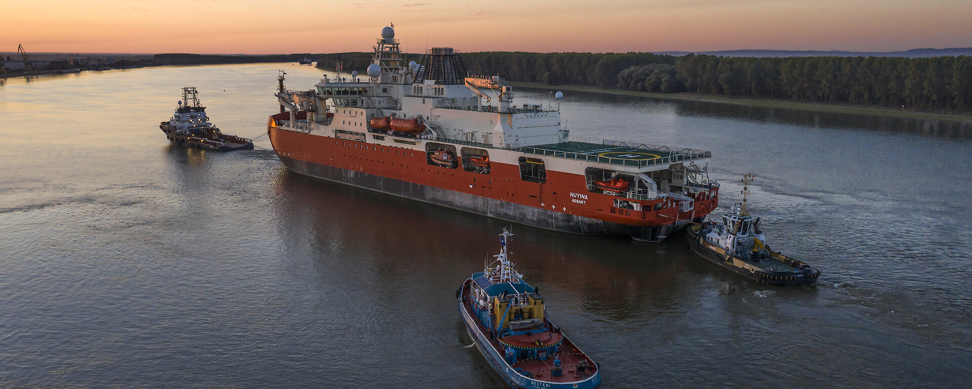 Three tugs guide icebreaker along river