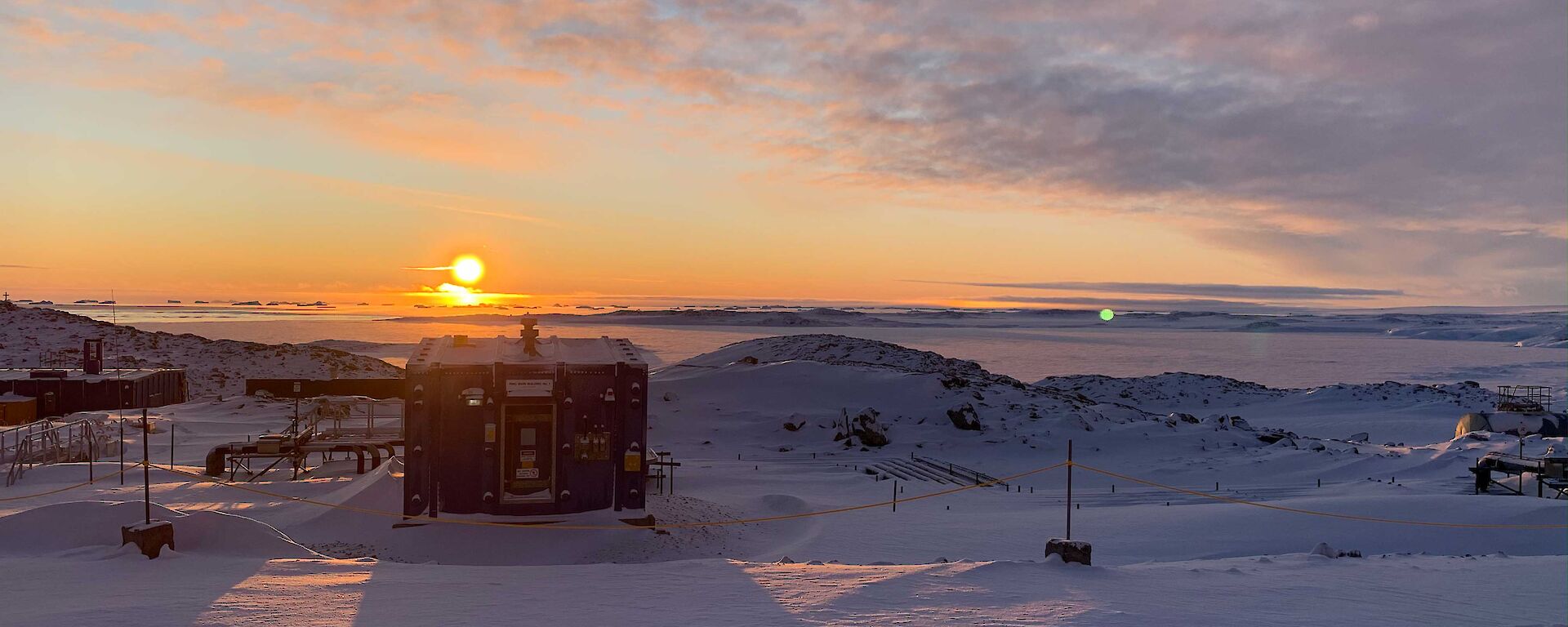 The blazing sun setting over distant icebergs