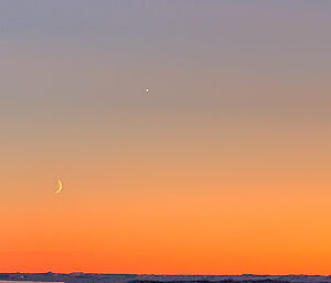 The crescent of the moon bathed in oranges from a sunrise