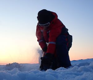 An expeditioner (Dan Dardha) cuts the Midwinter pool in the sea ice with a chainsaw