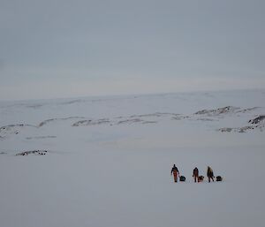 Expeditioners walking over the sea ice to Wilkes hauling their field packs in sleds
