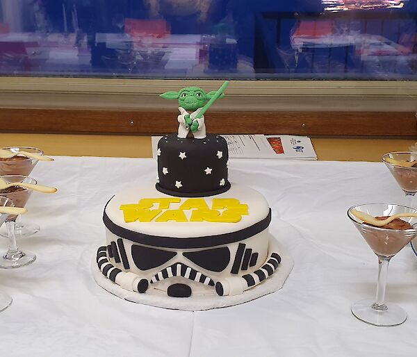 A Starwars themed cake is flanked on the dessert table by churros on one side and chocolate mousse on the other
