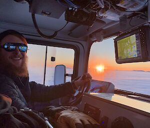 Smiling expeditioner driving a Hagglunds into the sunrise