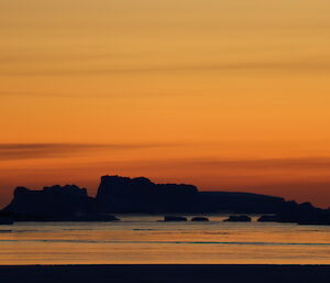 Silhouette of an iceberg in the distance at sunset
