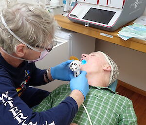 An expeditioner shines a blue light in the doctor's mouth