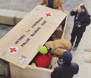 Four expeditioners standing around a large box marked return to Australia, polar medical unit