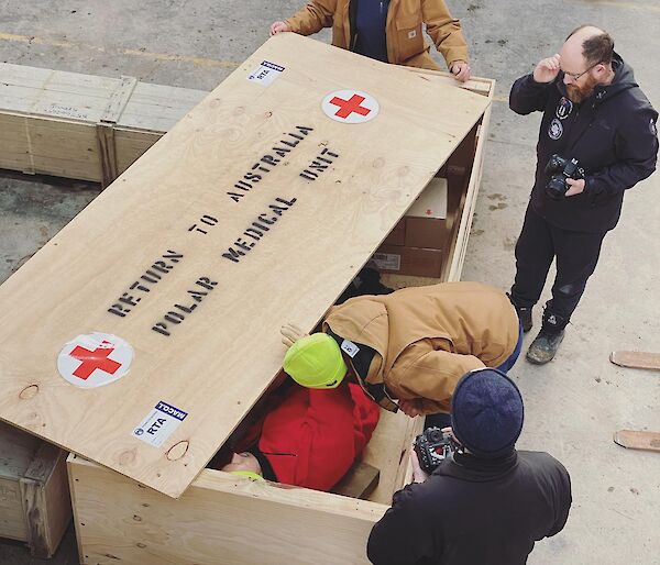 Four expeditioners standing around a large box marked return to Australia, polar medical unit