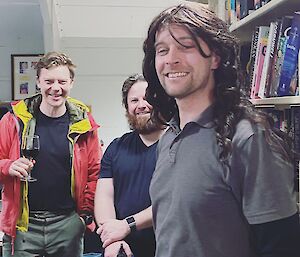 Three expeditioners smiling, one has on a long haired wig