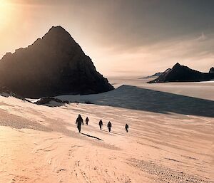 A group of expeditioners walking with a golden sun appearing above a mountain peak