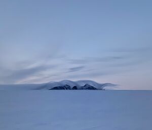 Portrait of a mountain in the distance with an interesting cloud covering it