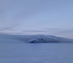 Portrait of a mountain in the distance with an interesting cloud covering it