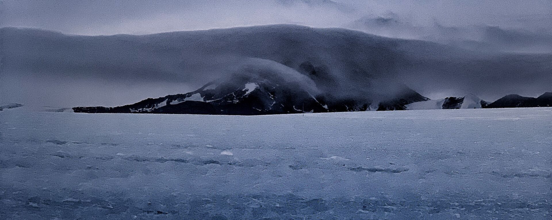 Portrait of a mountain in the distance with a cloud enveloping it