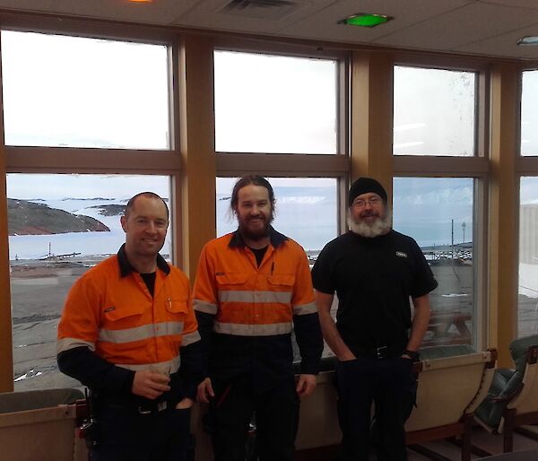 Three plumbers stand in the dining room with a view of the rest of the station in the background.