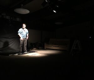 A man in a denim jacket standing in a spotlight on a dark stage