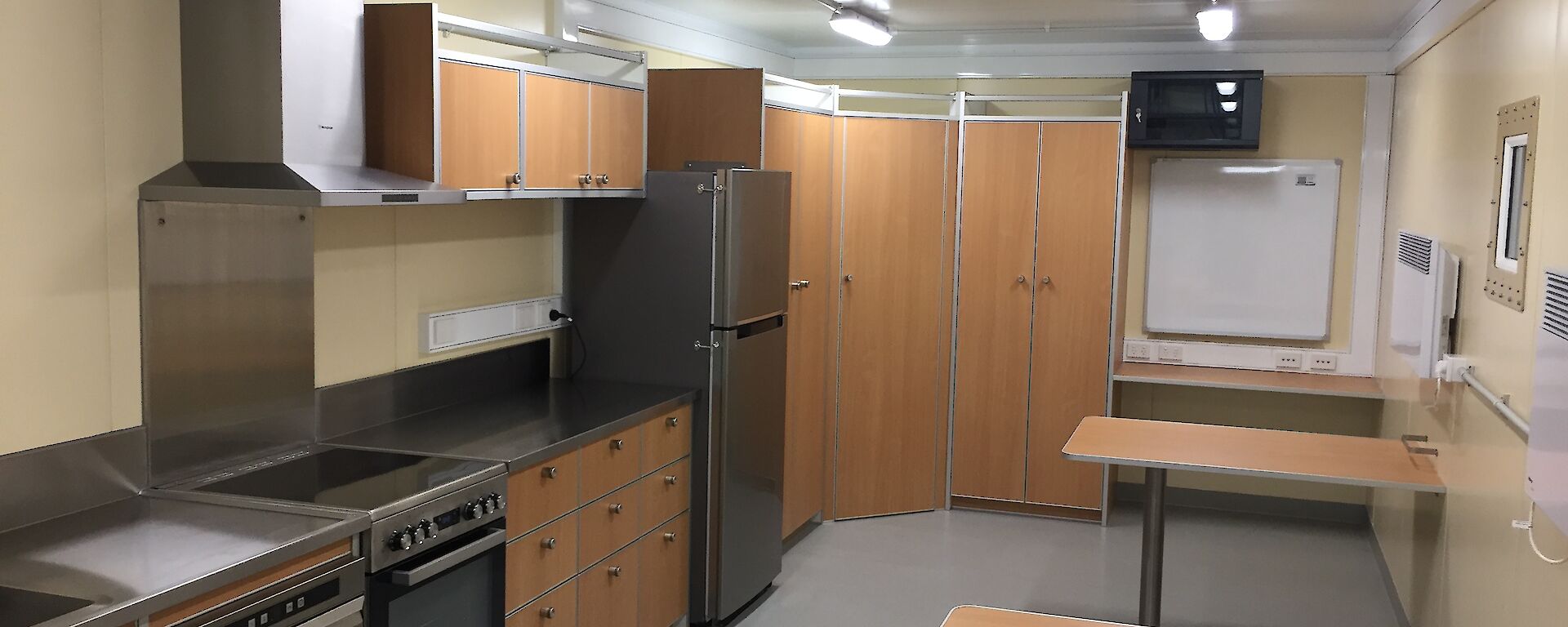 View of the kitchen in the traverse dining/living van, showing stainless steel appliances, cupboards and two dining tables.