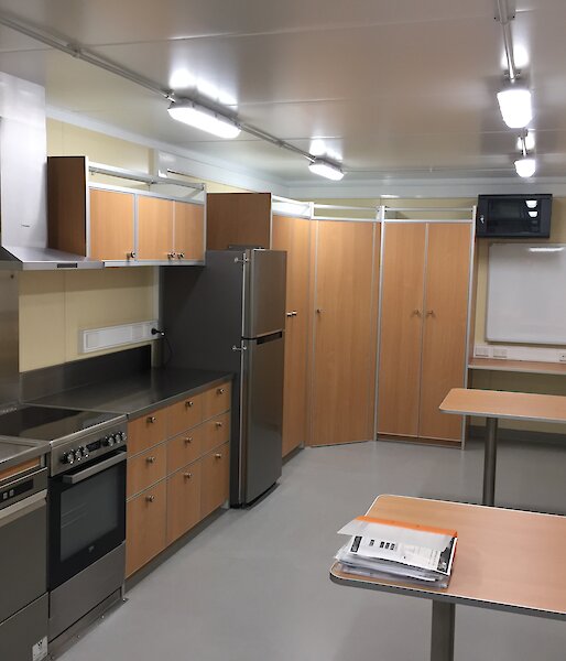 View of the kitchen in the traverse dining/living van, showing stainless steel appliances, cupboards and two dining tables.