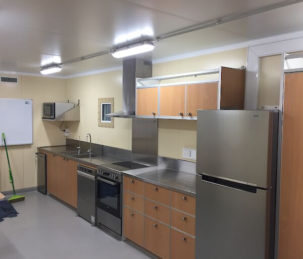 View of the kitchen in the traverse dining/living van showing the fridge, oven, dishwasher and stainless steel benchtops.