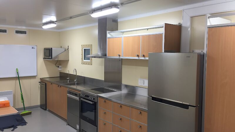 View of the kitchen in the traverse dining/living van showing the fridge, oven, dishwasher and stainless steel benchtops.