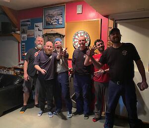 Maccas darts team line up in front of the darts board and pose for a photo.