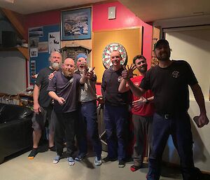 Maccas darts team line up in front of the darts board and pose for a photo.