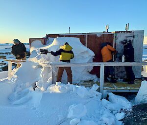 Men shoveling snow from the door of a hut