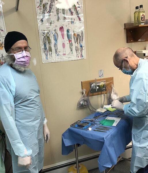 Two men in scrubs and face masks prepare the dentistry equipment in the medical room