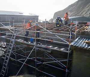 Mess building covered in scaffolding as five workers install replacement battens