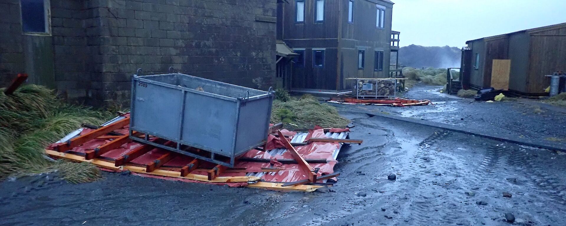 Station buildings Hass House and Cumptons Cottage with roofing debris on the ground.  Large metal container placed on roof material to hold it down