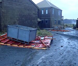 Station buildings Hass House and Cumptons Cottage with roofing debris on the ground.  Large metal container placed on roof material to hold it down