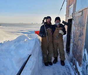 The entrance to the Wilkes hut dug out and the two bearded expeditioners who cleared it smiling to camera with ice picks and shovels over their shoulders