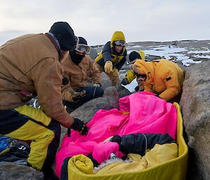 Injured expeditioner wrapped in bright sleeping bags on ground with rescuers around him