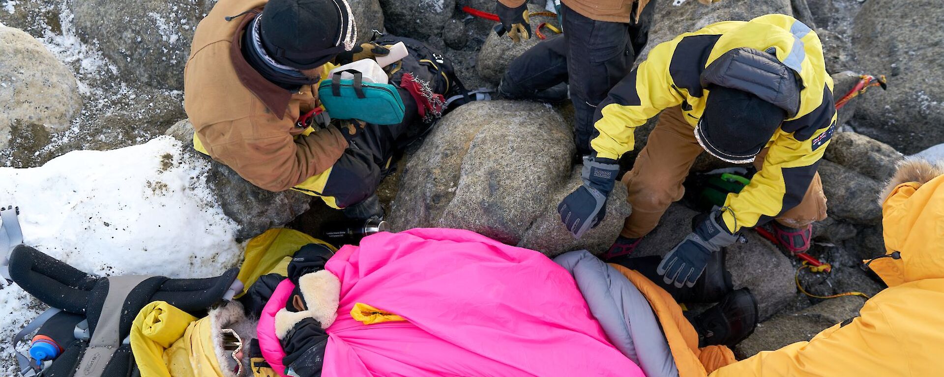 An aerial shot looking down at the injured expeditioner, lying on the ground covered in warm sleeping bags.  Various rescuers around him