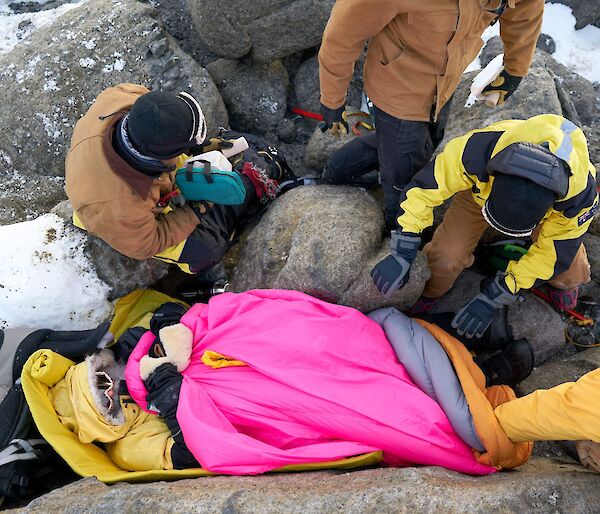 An aerial shot looking down at the injured expeditioner, lying on the ground covered in warm sleeping bags.  Various rescuers around him