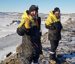 Two expeditioners smiling to camera with the water hose at their feet