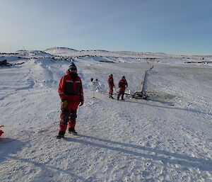 Three expeditioners smiling to camera standing on the frozen tarn
