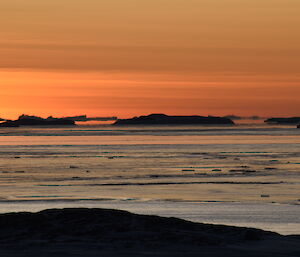 An orange winter sunset looking out to the East over the sea towards silhouetted icebergs
