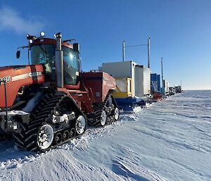 The Wilkins convoy with a red tractor in the foreground pulling colourful sleds packed with containers across the snow