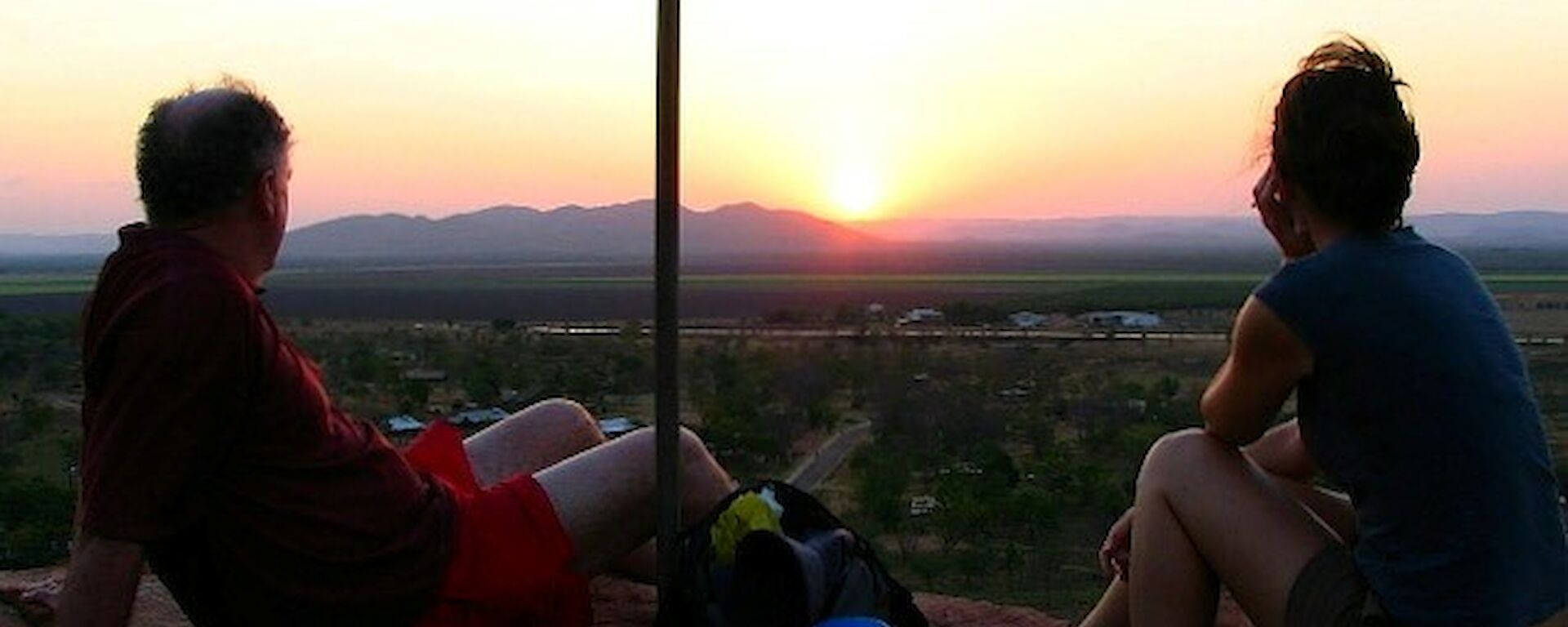 Two people sitting on a rock silouetted against a beautiful sunset