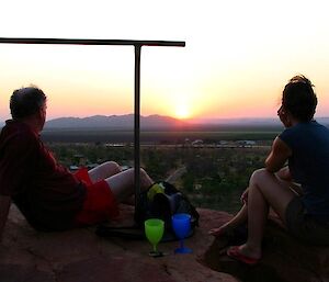 Two people sitting on a rock silouetted against a beautiful sunset