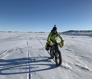 An expeditioner cycling towards the camera on the frozen sea.  The bike has special fat tyres and snow chains.