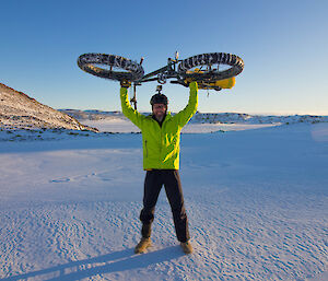 Rider standing on the ice,  holding a bike above their head