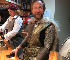 Two expeditioners behind the bar dressed as Bravehearts.  On wears a tartan hat with comedy ginger hair.